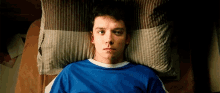 a young man in a blue shirt is laying on a bed with a pillow
