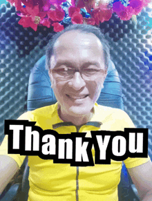 a man wearing glasses and a yellow shirt is smiling and says thank you