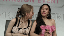 two women sitting next to each other in front of a sign that says 14.fri