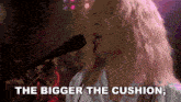 a woman singing into a microphone with the words " the bigger the cushion " above her