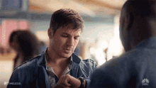 a man is looking at his watch while talking to another man in a crowded room .