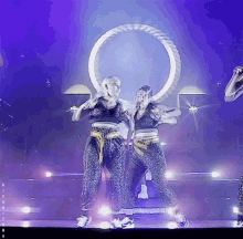 two women are dancing on a stage in front of a purple background