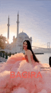 a woman in a pink dress stands in front of a mosque and bridge