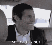 a man in a suit and tie is sitting in a car and smiling .