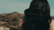a woman with long dark hair is standing in front of mountains