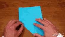 a person is holding a piece of blue paper on a wooden table and the words made in animatica are visible