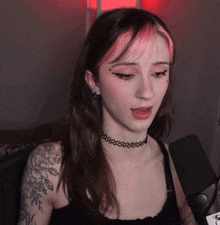 a woman with a choker and a tattoo on her arm talks into a microphone