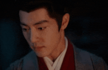 a close up of a man 's face in a dark room . he is wearing a red shirt and a grey jacket .