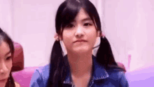 a girl with pigtails and a denim jacket is making a face .