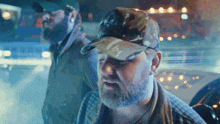 a man with a beard wearing a camo hat with the letter t on it