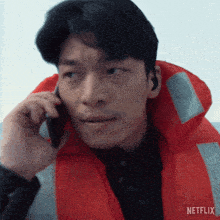 a man wearing an orange life jacket is talking on a cell phone with a netflix logo in the background