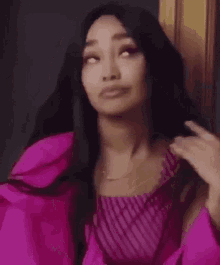 the woman is wearing a pink top and a pink jacket and is holding her hair .