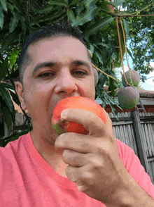 a man in a pink shirt is eating a mango outside