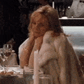 a woman in a fur coat is sitting at a table with a candle in a restaurant .