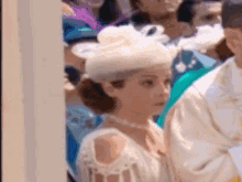 a woman in a white hat and pearls is standing in a crowd of people .