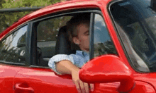 a man is driving a red sports car with his hand on the door .