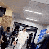 a man is holding a pair of shoes and talking into a microphone while walking down a hallway .