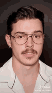a young man with glasses and a mustache is wearing a white shirt and earrings .