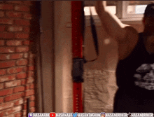 a man in a black tank top is doing pull ups in front of a red brick wall