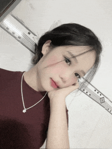 a girl wearing a necklace and a maroon shirt is taking a selfie