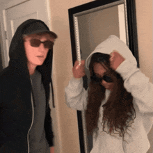 a man in a hoodie and sunglasses stands next to a woman in a hoodie
