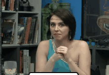 a woman in a blue dress is sitting in front of a bookshelf with books on it