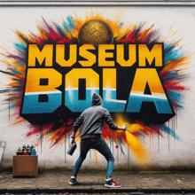 a man spray paints a wall with the words museum bola