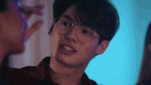 a young man wearing glasses and a plaid shirt is standing next to another man .