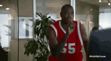 a man wearing a red basketball jersey with the number 65 on it is standing in front of a window .