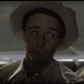 a man wearing a hat and a white shirt looks at the camera