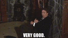 a man in a suit and tie is sitting on the floor with the words very good below him