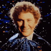 a man with curly hair is smiling and wearing a polka dot bow tie