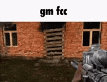 a person is holding a gun in front of a brick building with the words gm fcc on the bottom .