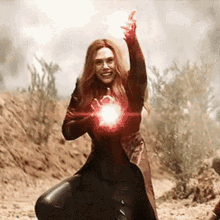 scarlet witch is holding a red light in her hand while standing in the dirt .