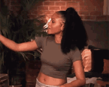 a woman in a crop top is dancing in a room with a brick wall .