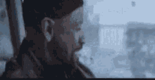 a man with a beard is looking out of a window while smoking a cigarette .