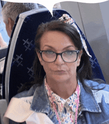 a woman wearing glasses and a denim jacket sits on a blue seat