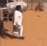 a man in a white robe is walking down a dirt road with a large bag on his back .