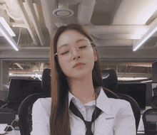 a woman wearing glasses and a tie sits in an office with her eyes closed