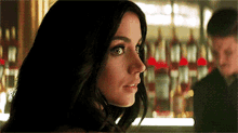 a woman is standing in front of a bar with bottles of alcohol in the background .