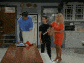 a woman in a red dress is standing next to a man and a woman in a kitchen