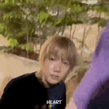 a young boy wearing a black shirt with the word heart on it is standing next to a purple shirt .