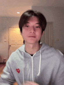 a man wearing a grey hoodie with a red heart on the front