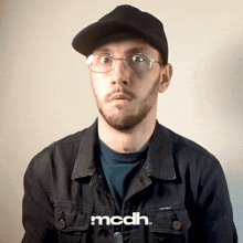a man wearing glasses and a hat has the word mcdh on his shirt