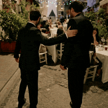 two men in suits are hugging each other in front of a crowd of people sitting at tables
