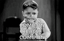 a little boy is sitting at a desk with his hand on his chin and the words `` come on really come on '' written on it .