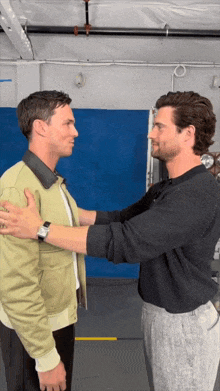 two men are hugging each other in a room with a blue wall behind them