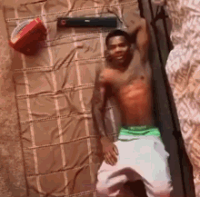 a man without a shirt is laying on a bed with a basketball and a speaker .