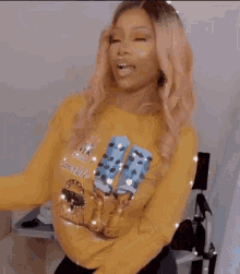 a woman wearing a yellow sweatshirt with a picture of a woman on it is dancing with her arms in the air .