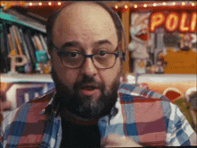 a man wearing glasses and a plaid shirt stands in front of a neon sign that says poli